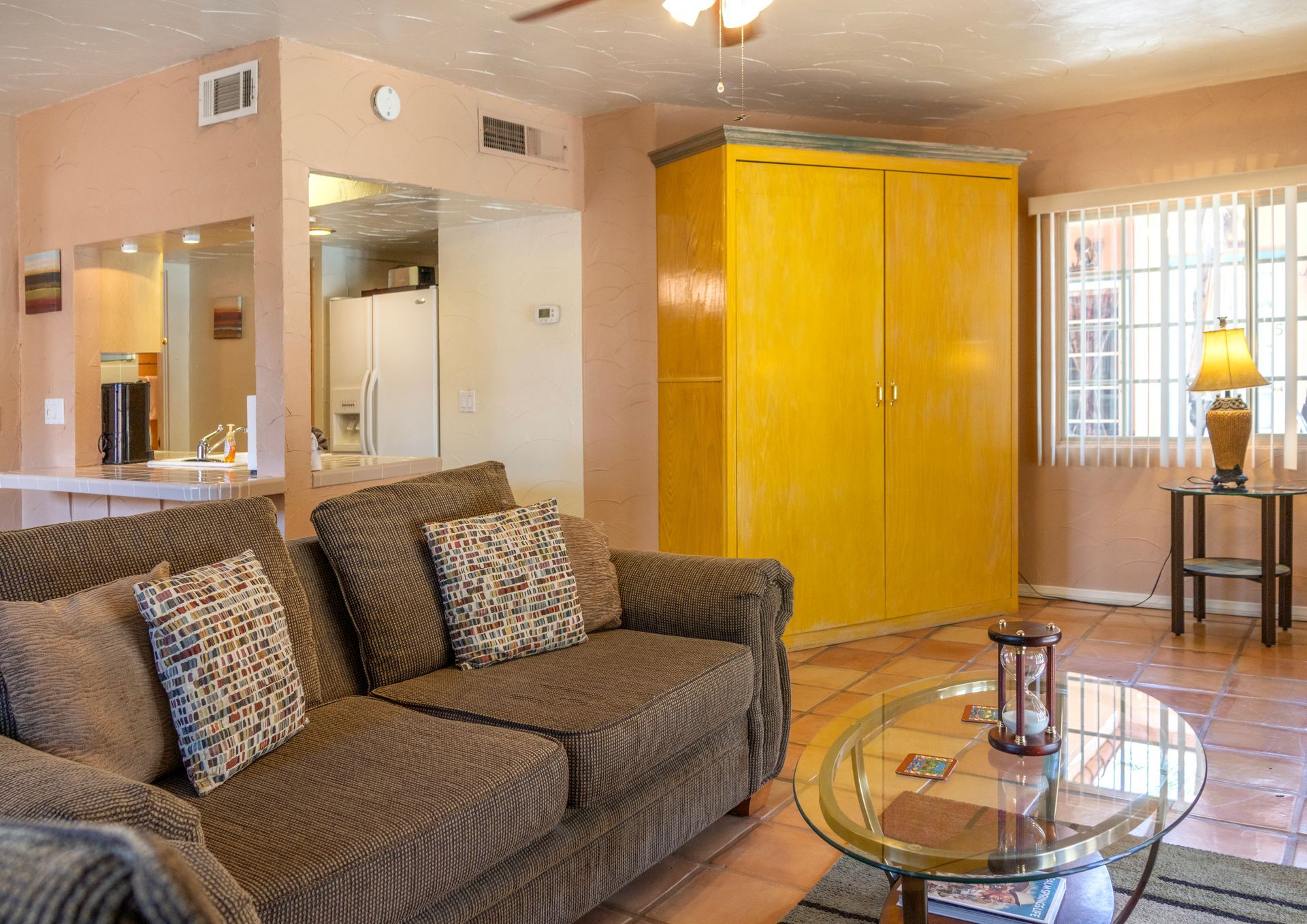 Living room with brown couch, yellow cabinet, round glass coffee table, and window.