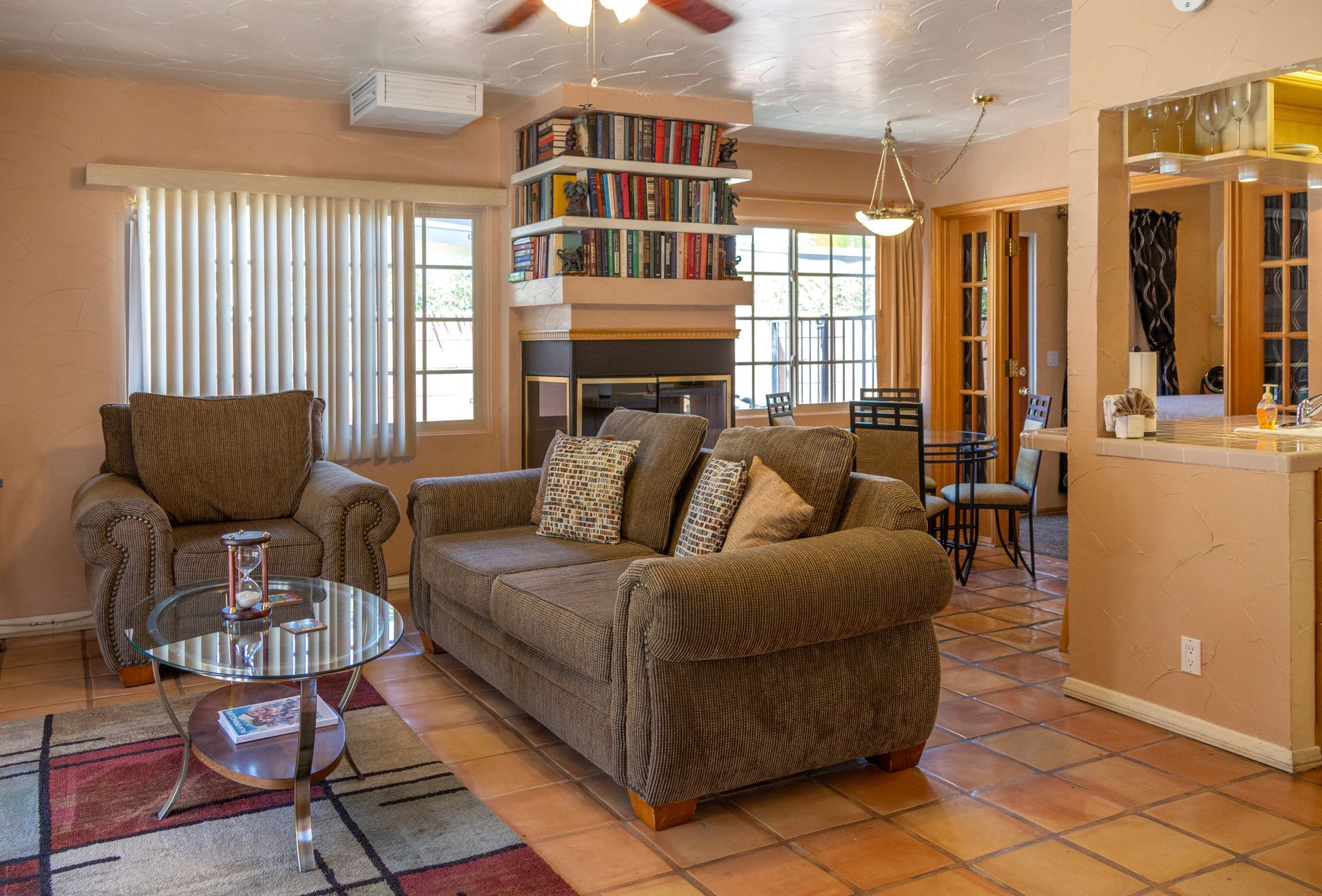Living room with brown sofa, armchair, glass coffee table, fireplace, and bookshelf.