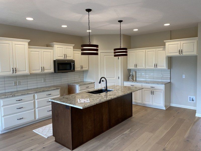 Bright kitchen with white cabinets, dark island, granite countertops, and wood floor.