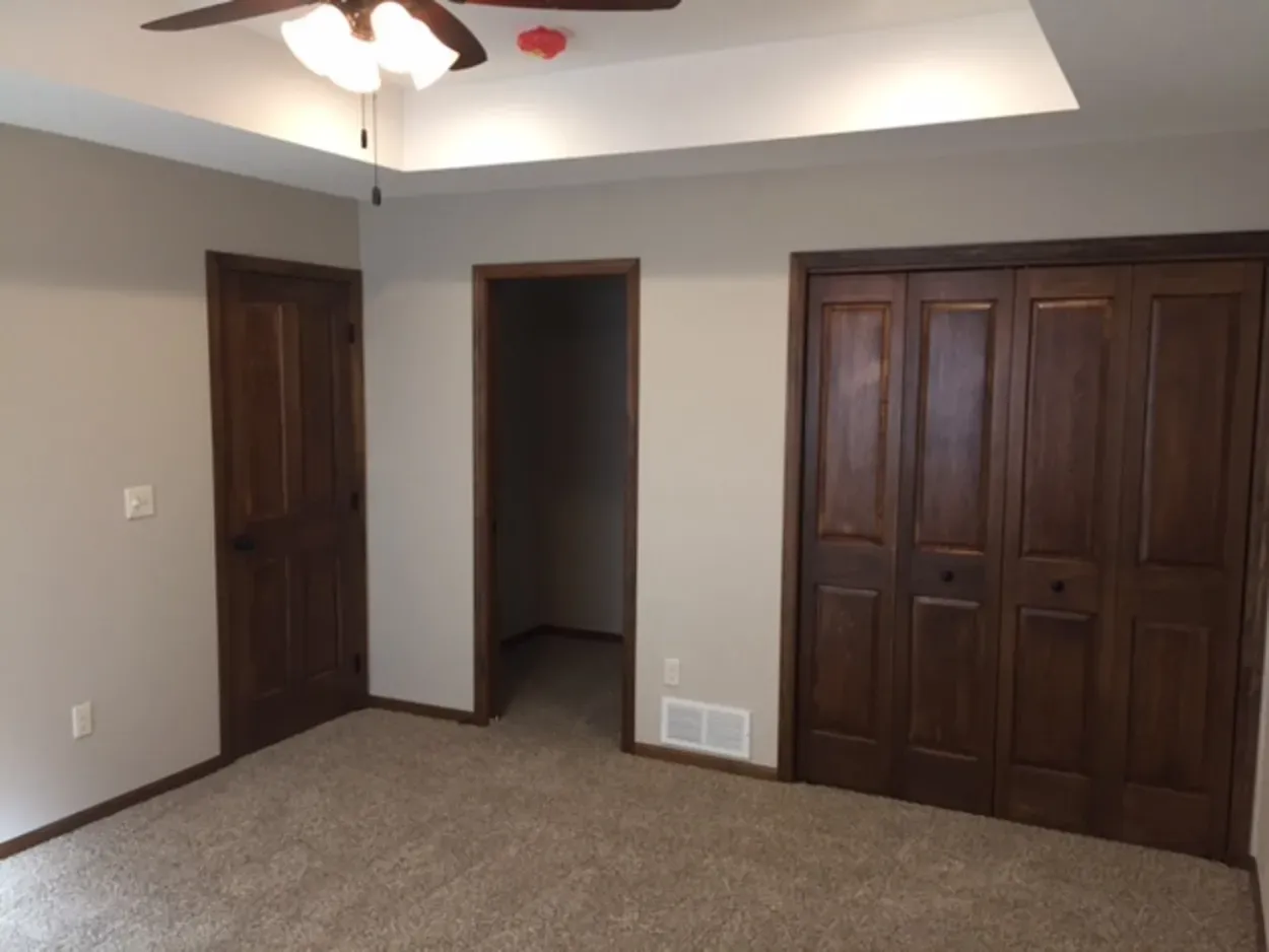 Bedroom with brown wooden doors, closet, and beige walls and carpet.