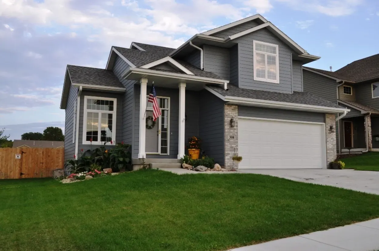 Blue house with white trim, a garage, green lawn, and an American flag.