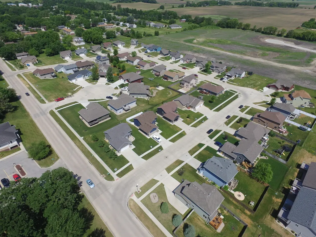 Aerial view of a suburban neighborhood with houses, streets, and green lawns on a sunny day.