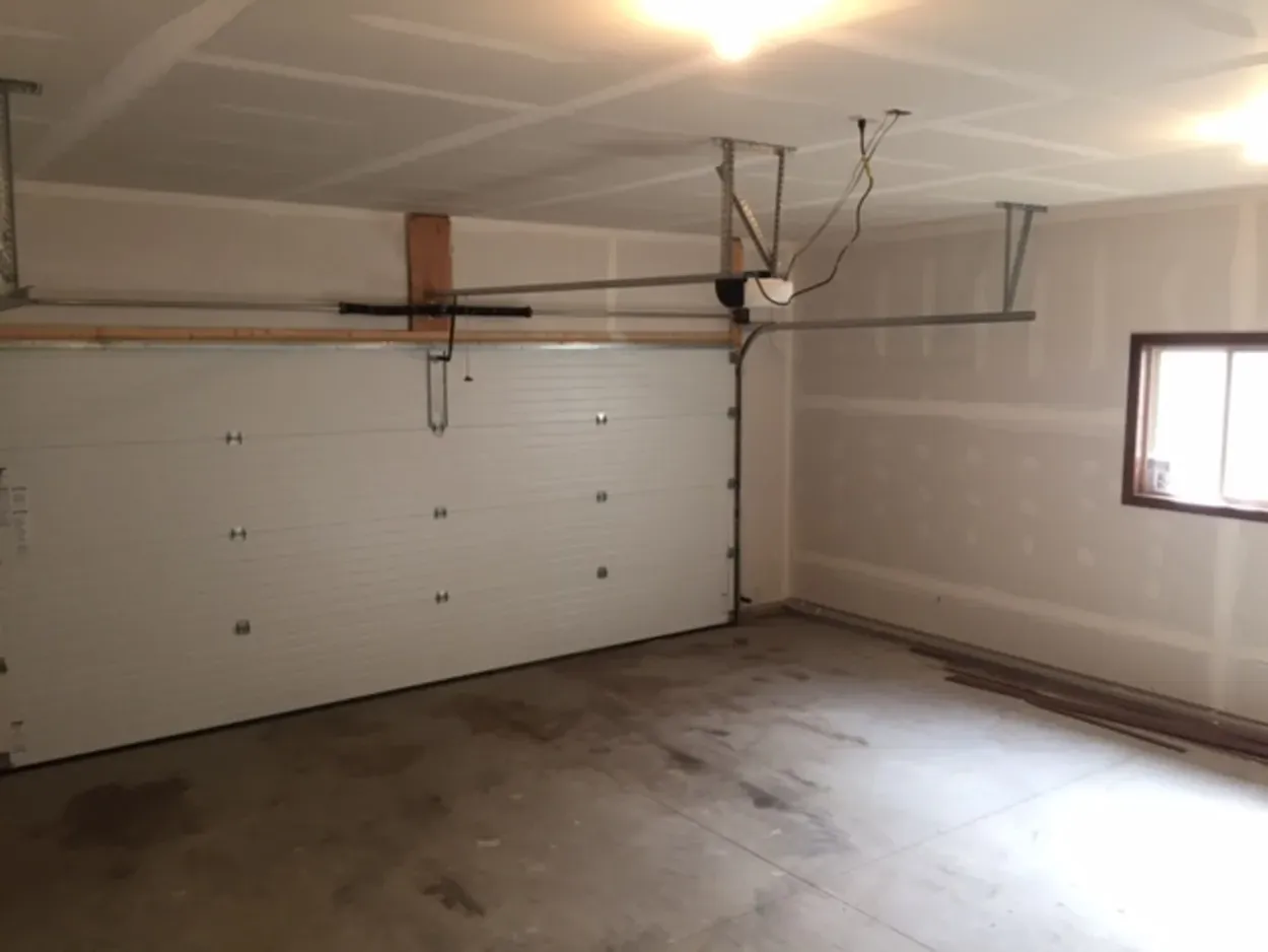 A garage interior with a closed white door, unfinished drywall, and concrete floor.