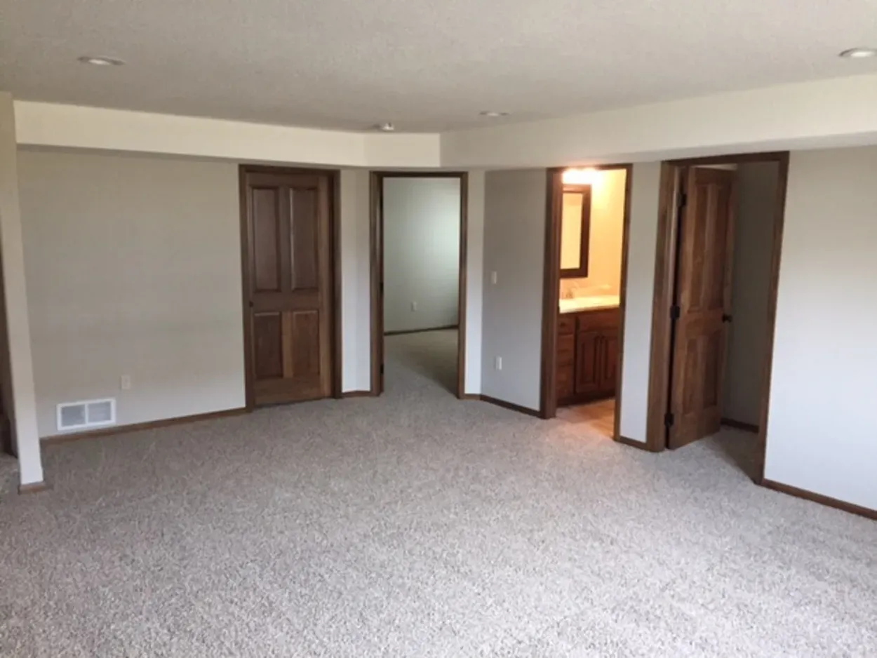 Empty room with beige carpet, light gray walls, brown doors and trim, and a small bathroom visible.