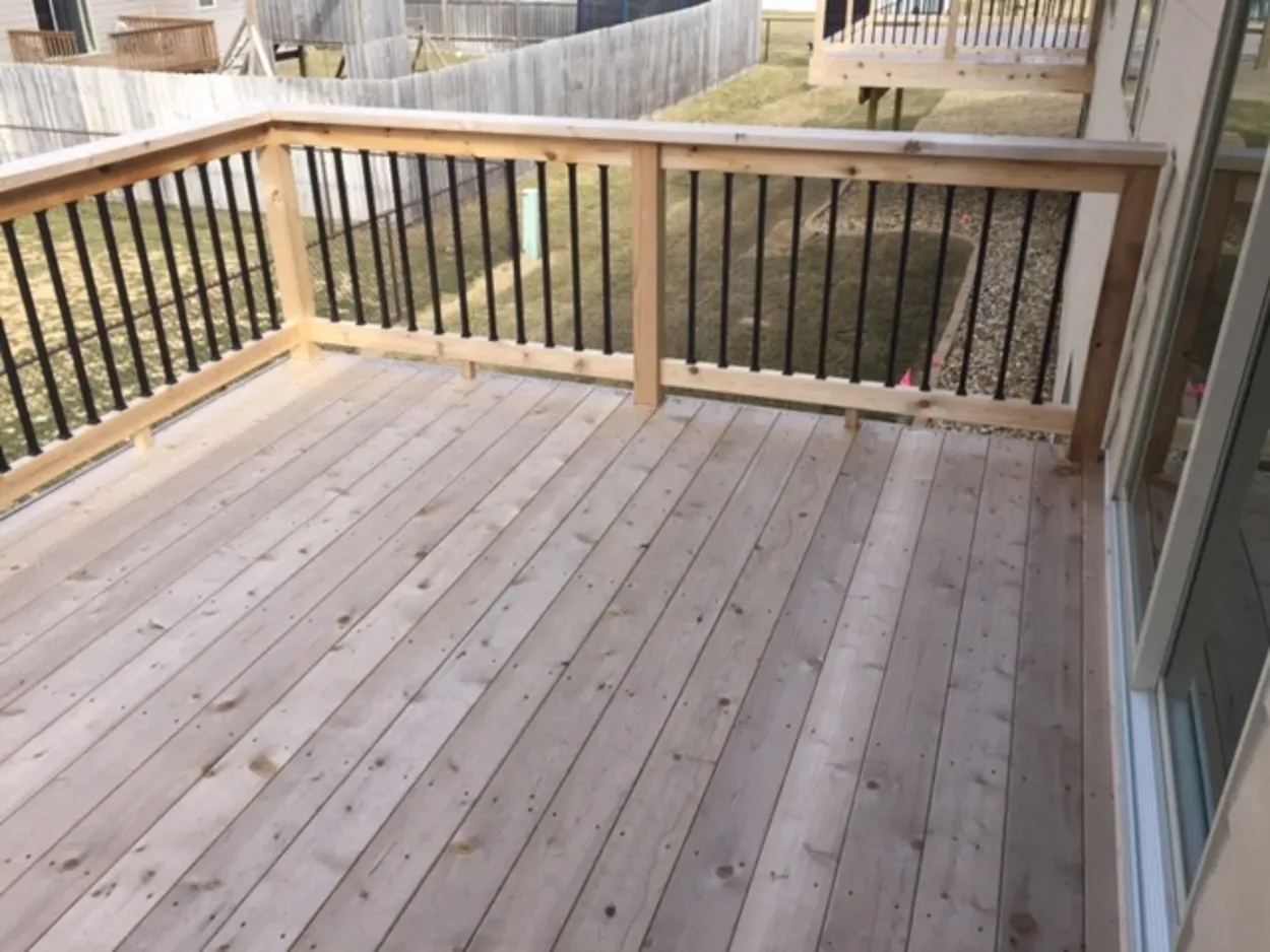 Wooden deck with light-colored boards, framed with railings and black vertical bars.
