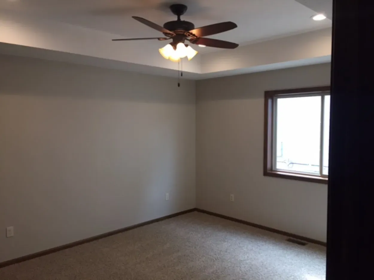 Empty bedroom with tan walls, brown carpet, and a ceiling fan.