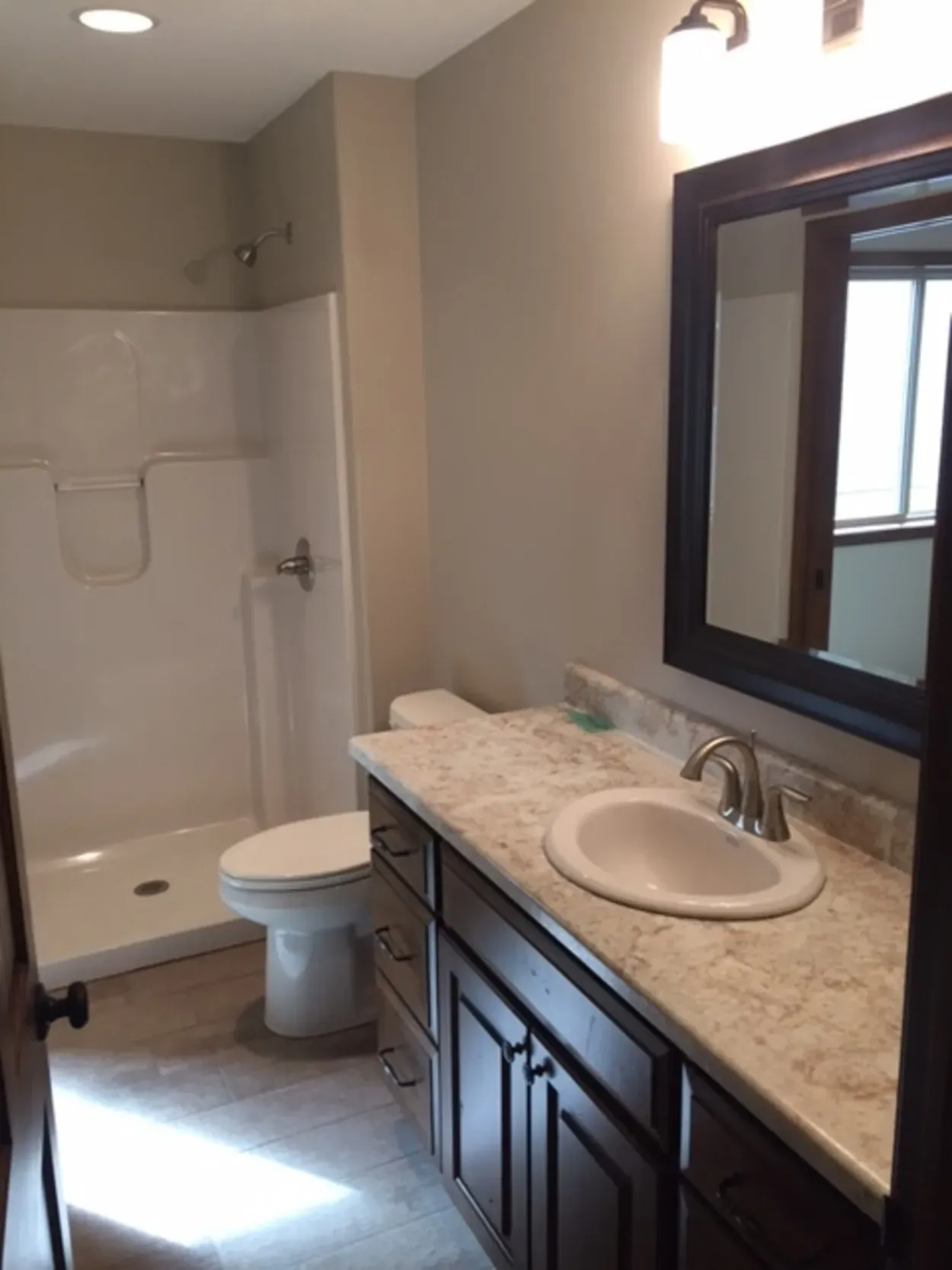 Bathroom with white shower, dark brown vanity, and large mirror.