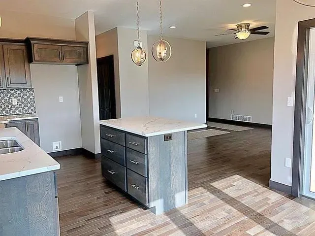 Modern kitchen with island, cabinets, and open layout to living area with hardwood floors.
