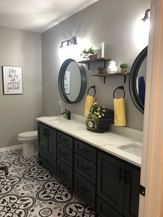 Bathroom with a black vanity, round mirrors, gray walls, and patterned tile floor.