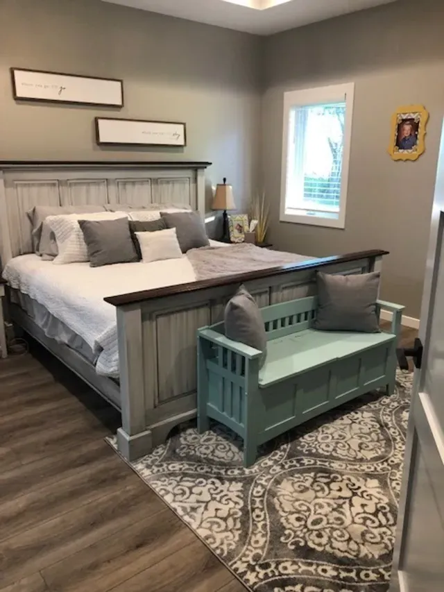 Bedroom with a large bed, light blue bench, area rug, and framed pictures.