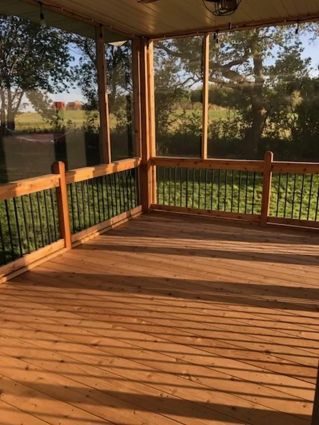 Wooden screened-in porch with railing, casting shadows from the slatted floor.