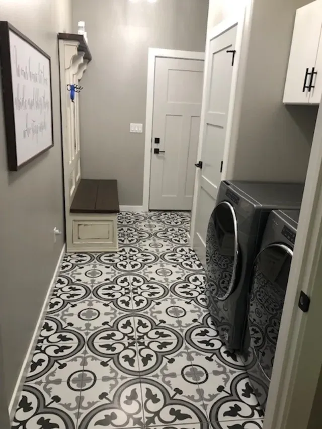 Laundry room with decorative floor tiles, washer and dryer, bench, and wall art.