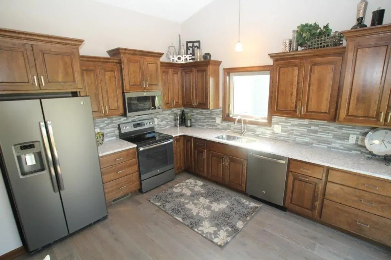 A kitchen with wooden cabinets, stainless steel appliances, light countertops, and a grey rug.