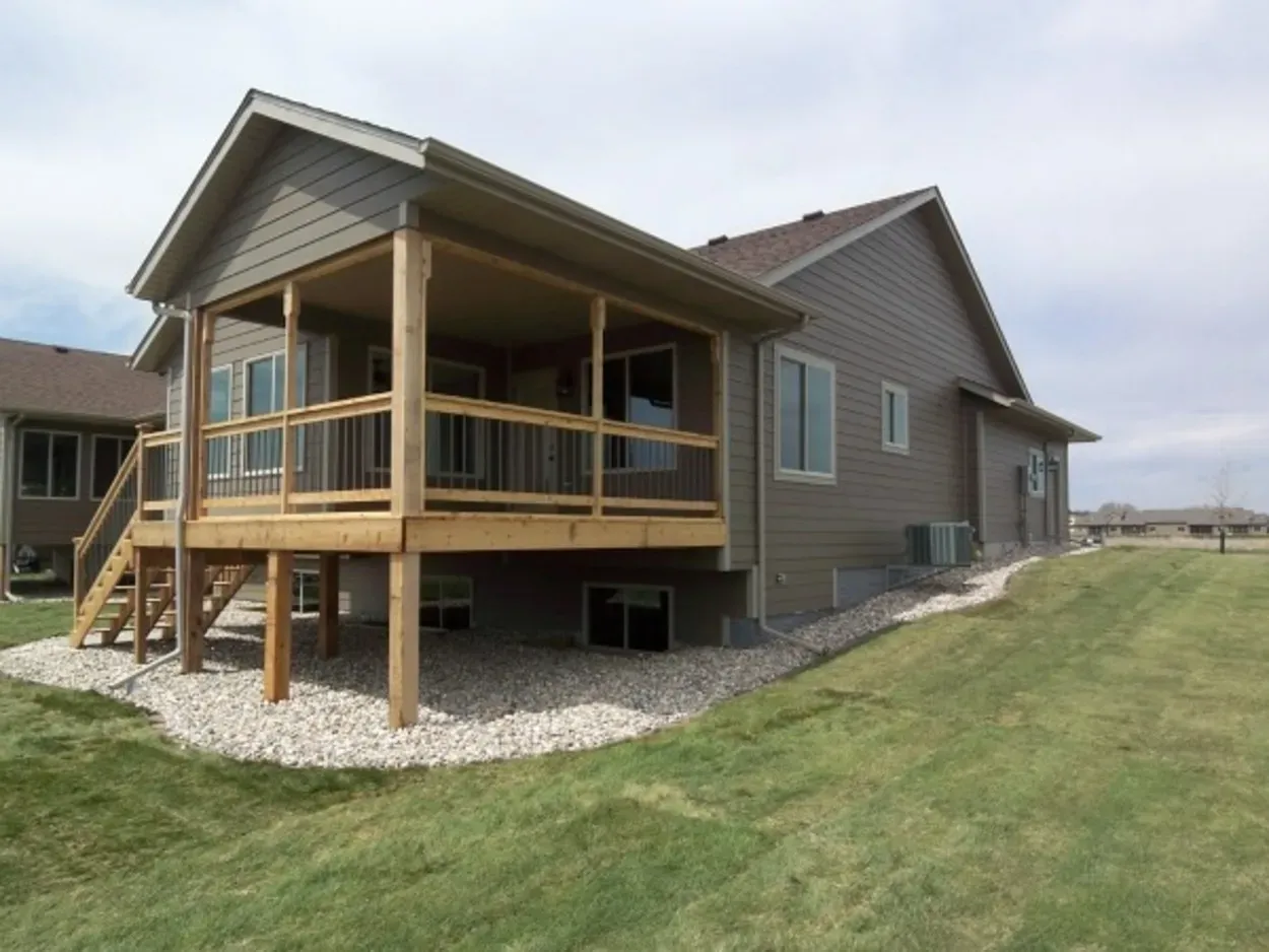 House with a wooden deck and screened porch, light brown siding, green lawn.
