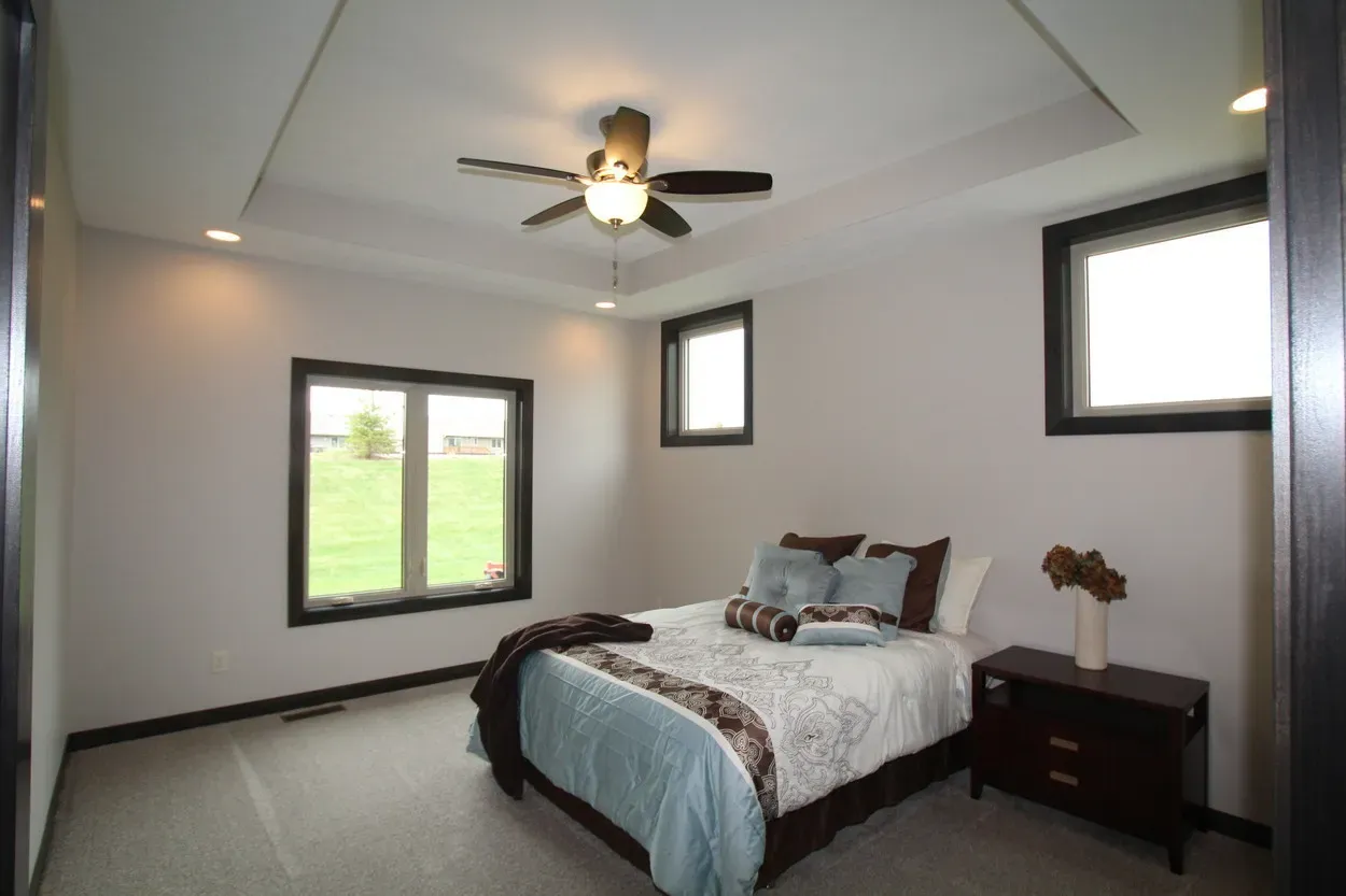 Bedroom with bed, windows, ceiling fan, and nightstand.