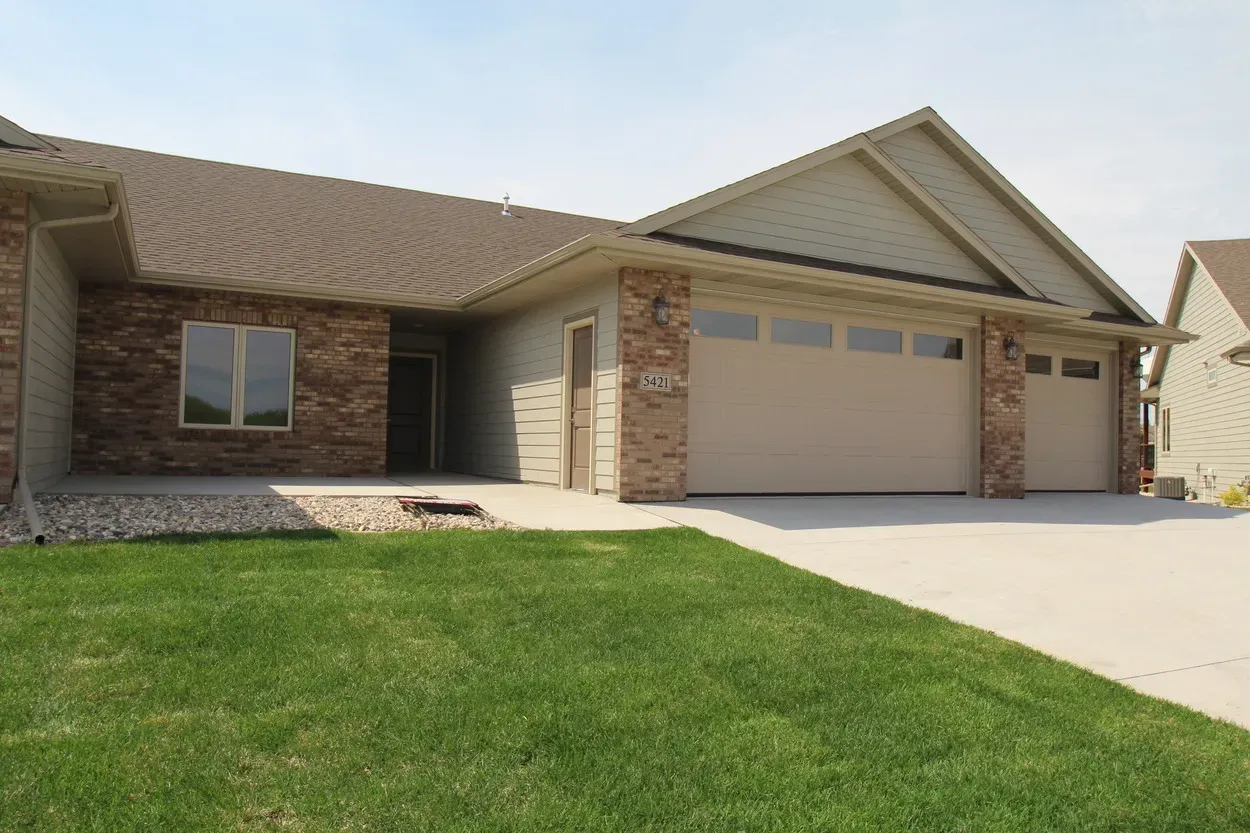 A light-colored house with a brick facade and a two-car garage with a concrete driveway.