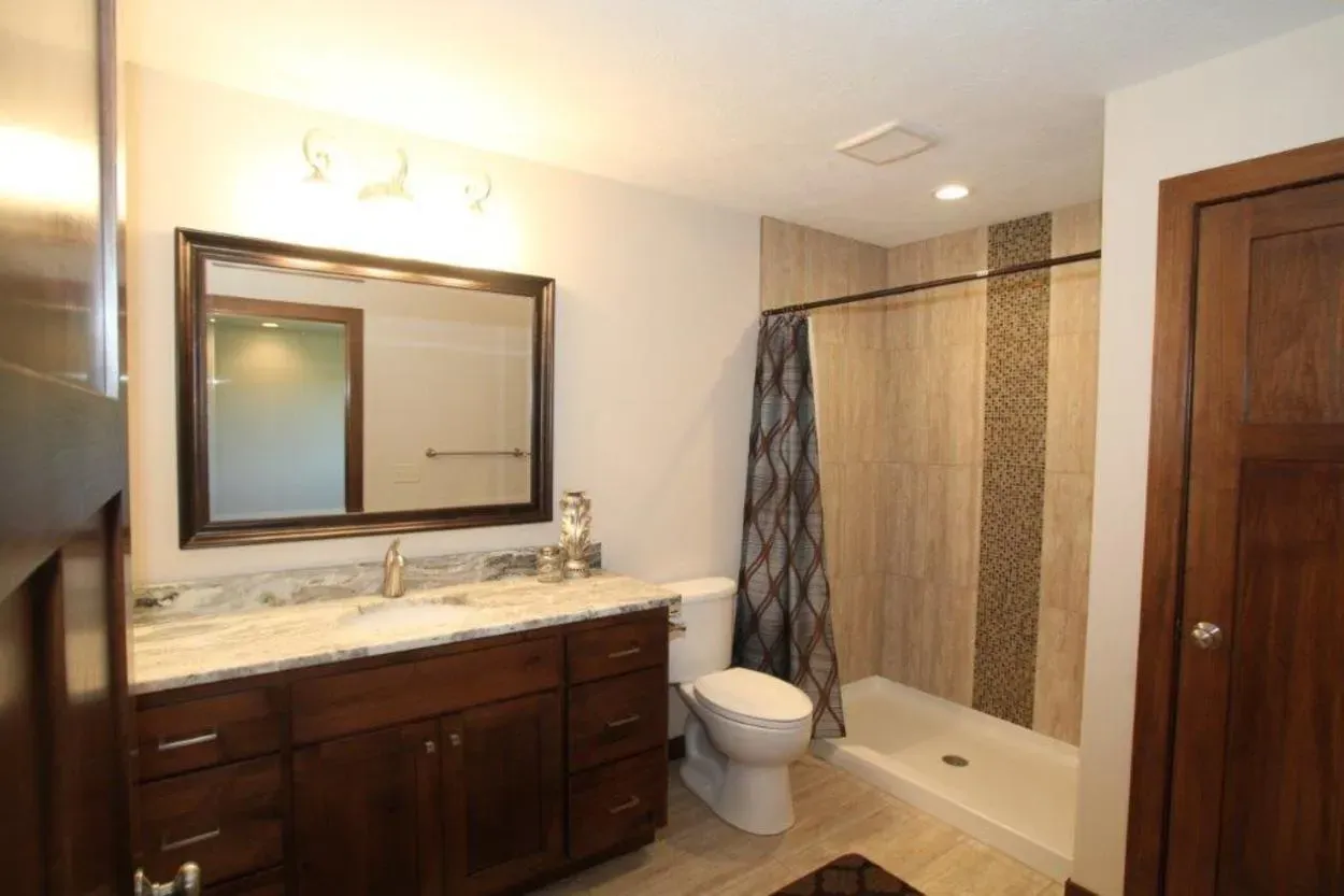 Bathroom with dark wood vanity, light countertop, large mirror, tile shower, and dark wood door.