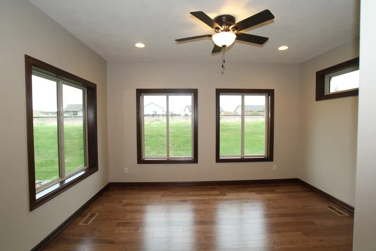 Empty room with wood floors, brown window frames, and ceiling fan. 