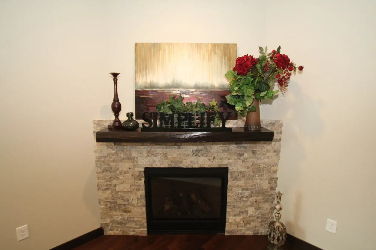 Fireplace with stone facade, dark mantel, artwork, flowers, and candles.