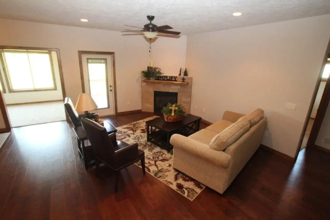 Living room with fireplace, beige sofa, dark chairs, dark wood floor, and area rug.