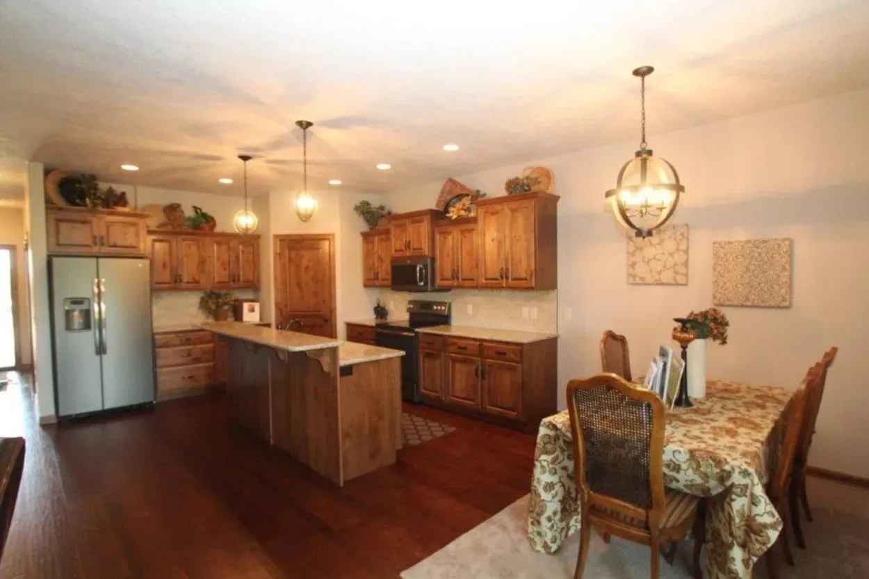 Kitchen with wooden cabinets, island, dining table, chandelier, and stainless steel refrigerator.