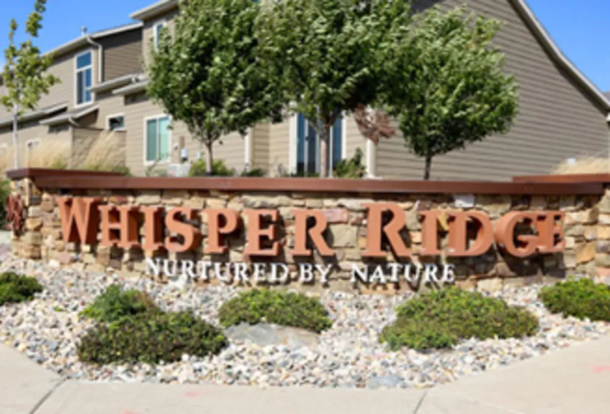 Sign for Whisper Ridge, a housing development, with landscaping and stone wall. 