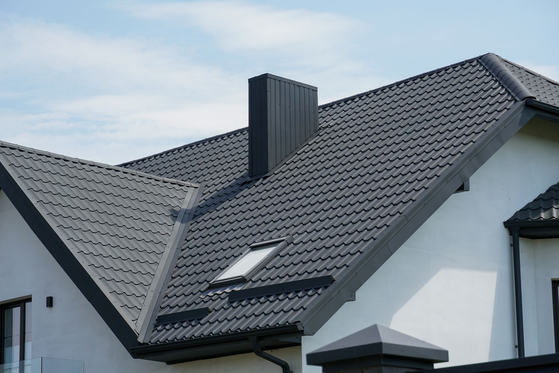 Dark gray tiled roof on a white house, with a chimney and skylight. 