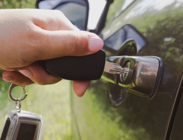 Hand with car key unlocking a car door. Green car, sunny outdoor setting.