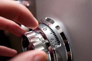 Hand turning a combination dial on a safe; silver metal, close-up.
