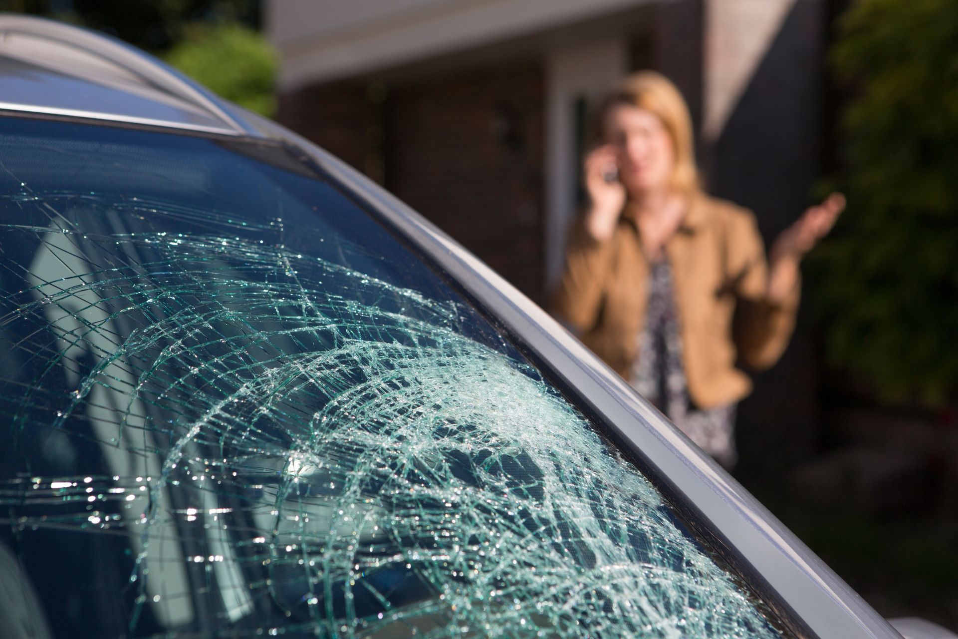 a woman is talking on a cell phone in front of a car with a broken windshield