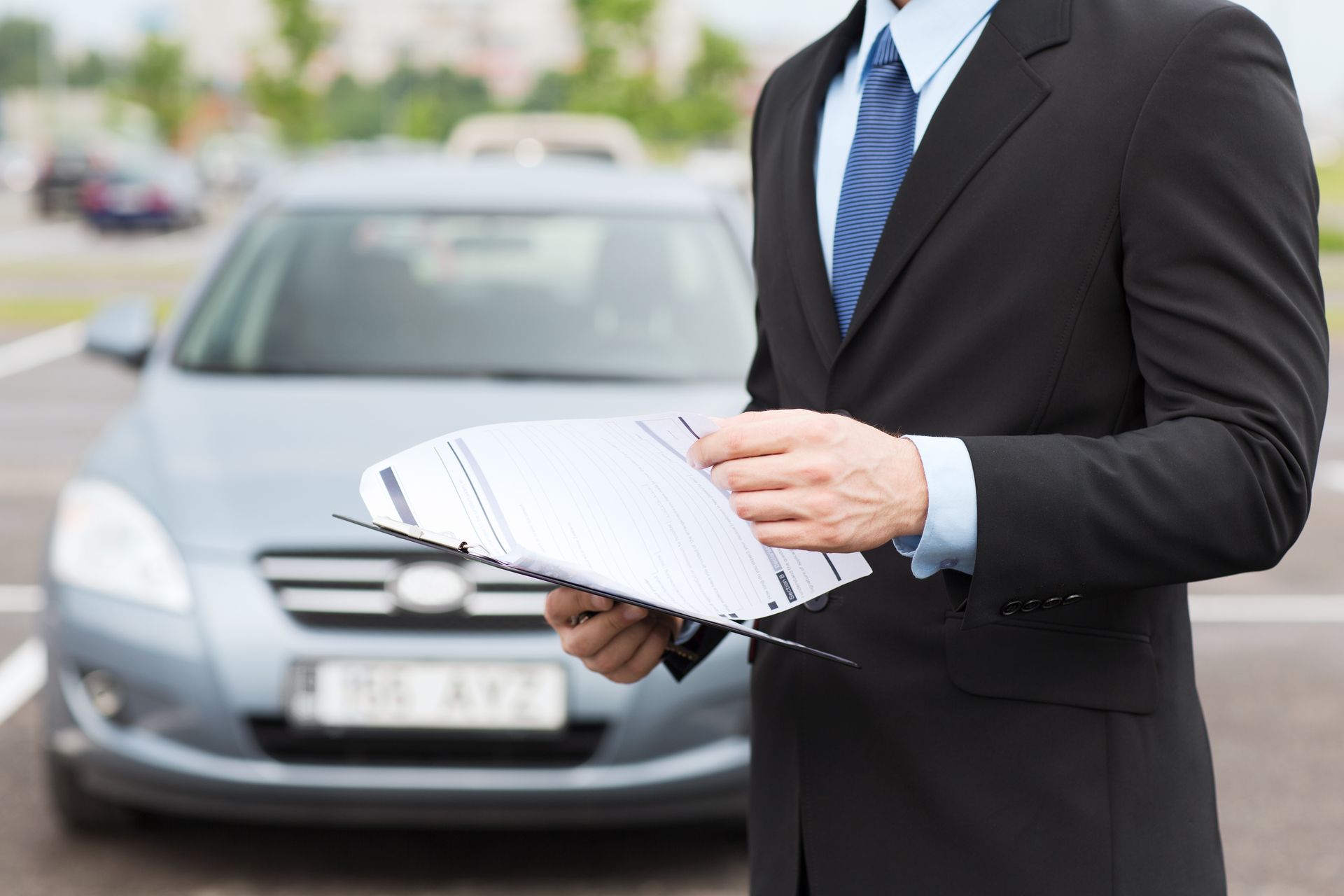 a man in a suit and tie is holding a clipboard in front of a car