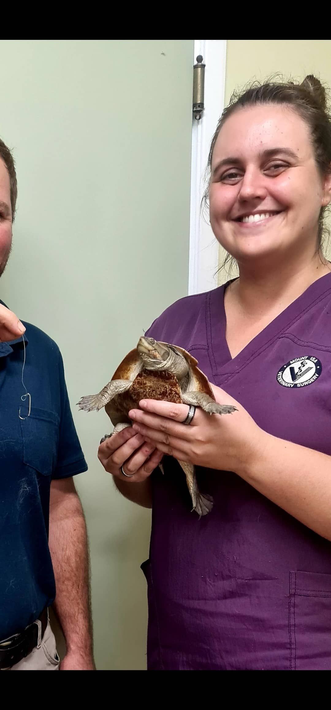 A Smiling Woman in Purple Scrubs Holds a Tortoise; Another Person Stands Beside Them — Mount Isa Veterinary Surgery In Ryan, QLD