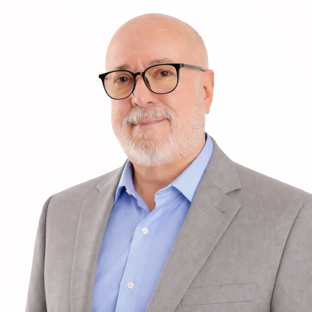 Una persona con la cabeza rapada y barba gris, que lleva gafas, una camisa de cuello azul claro y un blazer gris.