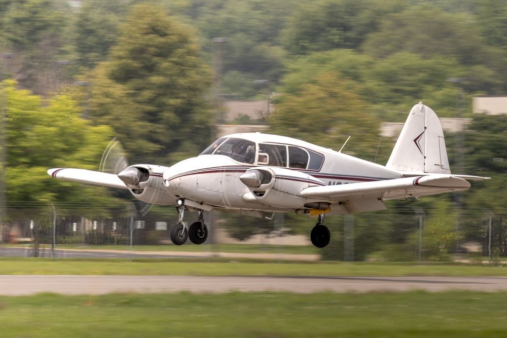 White twin-engine prop plane landing on a runway with trees blurred in the background