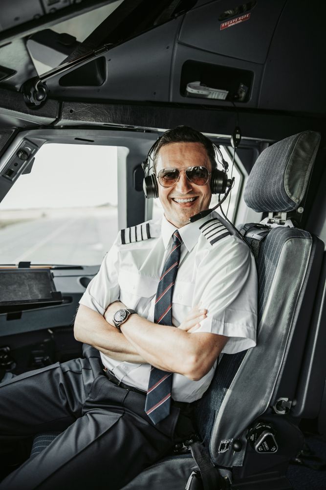 Pilot in the cockpit smiling with arms crossed, wearing sunglasses, headset, and uniform.