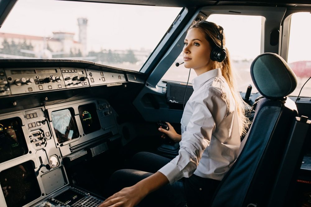 A female pilot is sitting in the cockpit of an airplane.