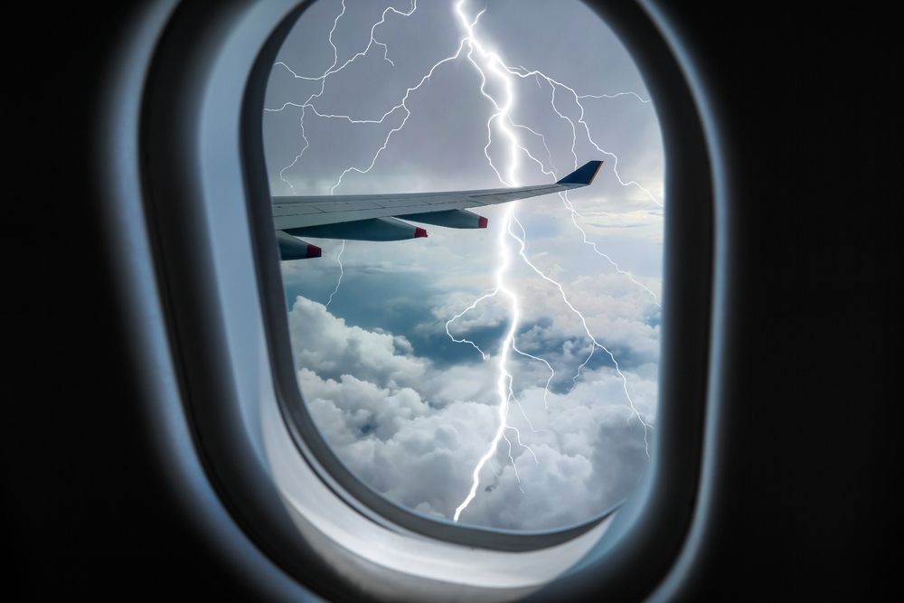 Lightning is visible through the window of an airplane.