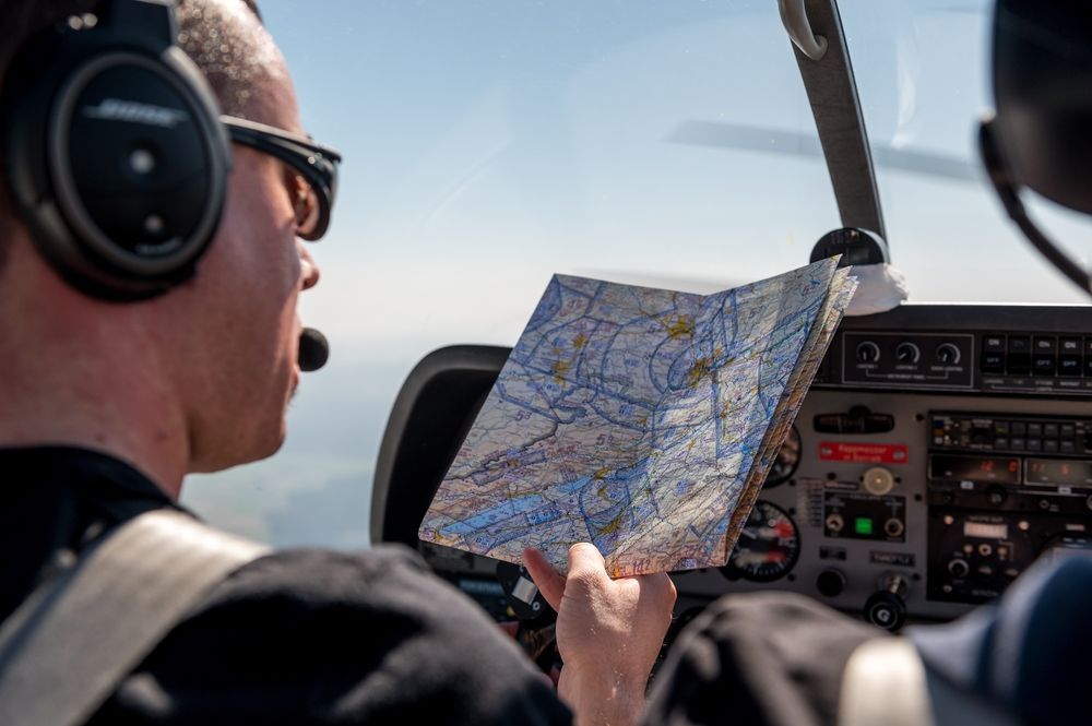 A man wearing headphones is looking at a map while flying an airplane.