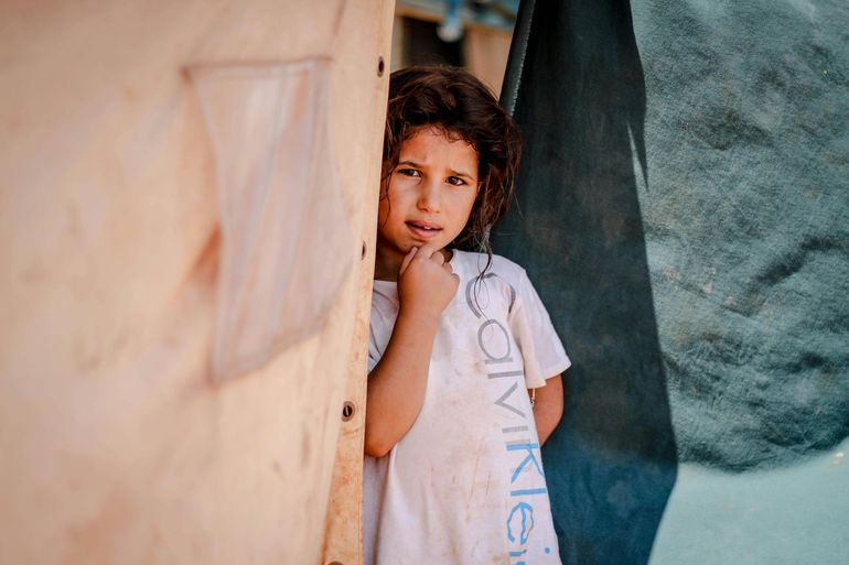 A little girl is peeking out from behind a wooden wall.