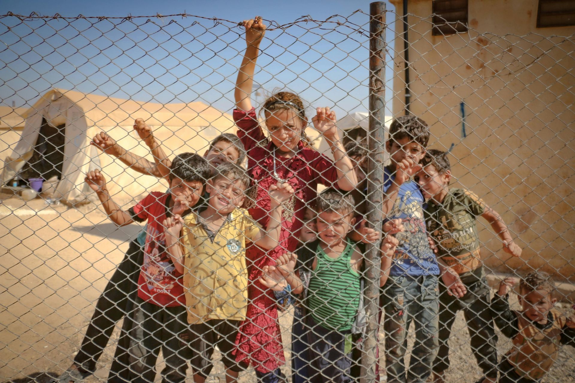 A group of children are standing behind a chain link fence.