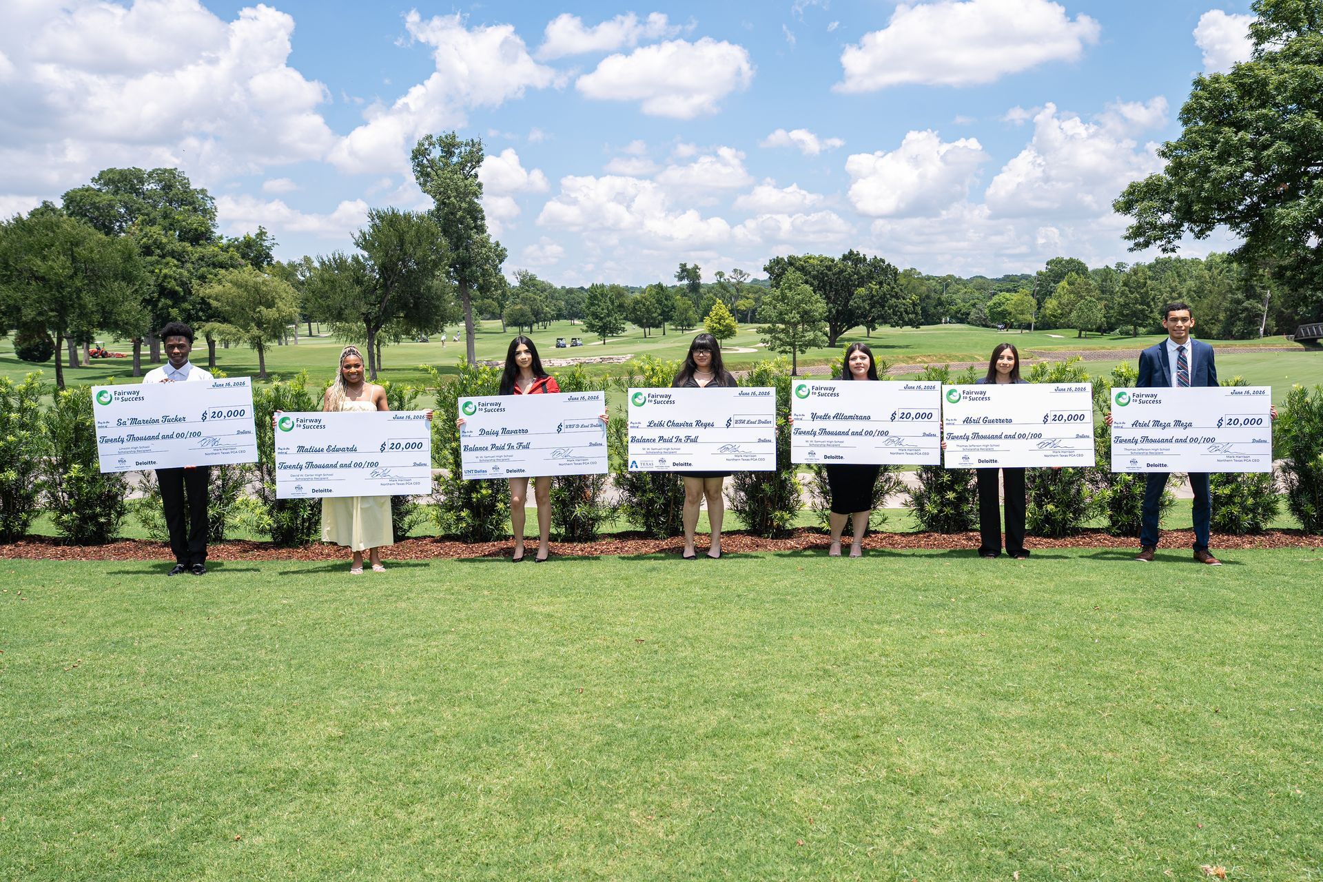 People holding protest signs on a grassy lawn in front of a building with trees behind them