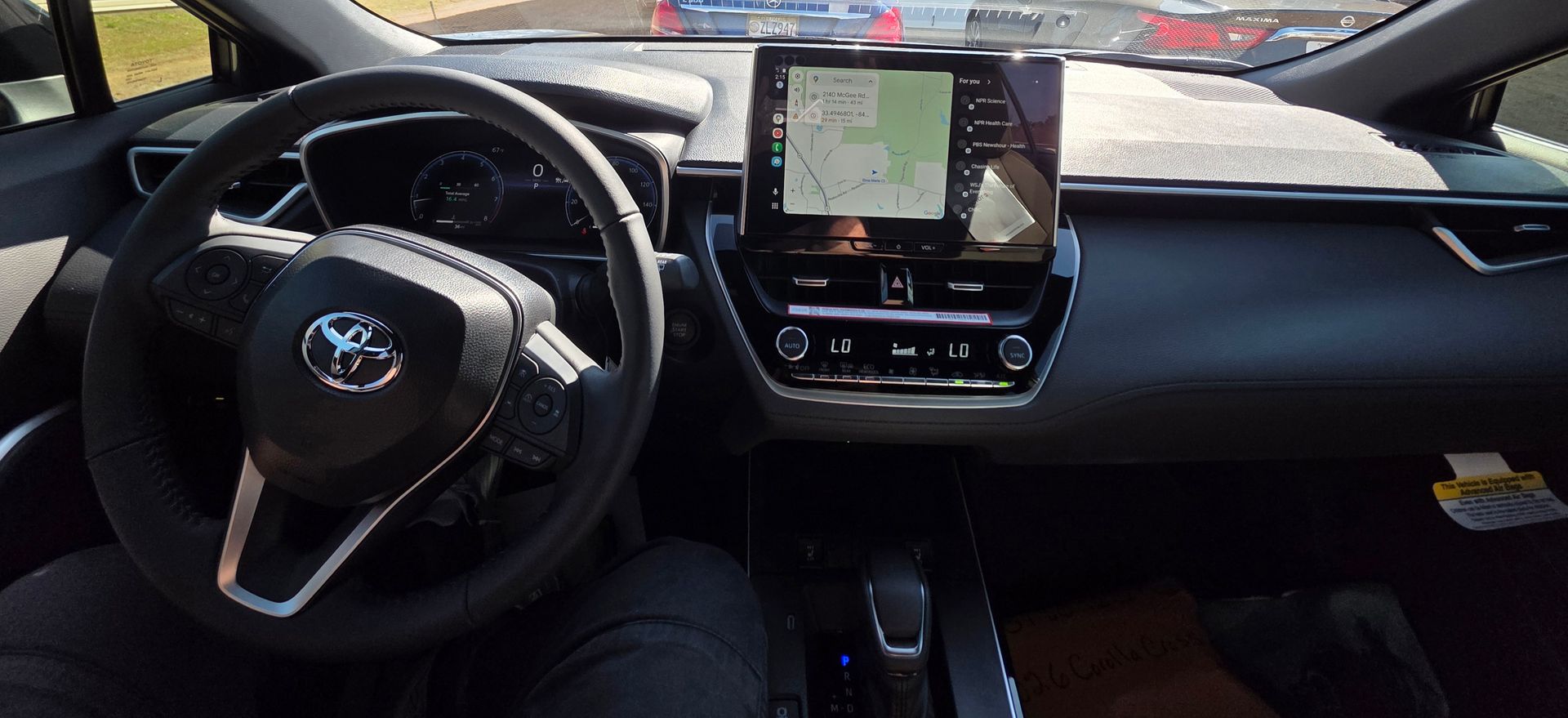 The driver's seat view of a Toyota car interior, showing the steering wheel, digital dashboard, and infotainment screen.