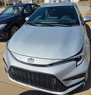 Silver Toyota Corolla, front view, parked on driveway next to a dark blue car, sunny outdoor setting.