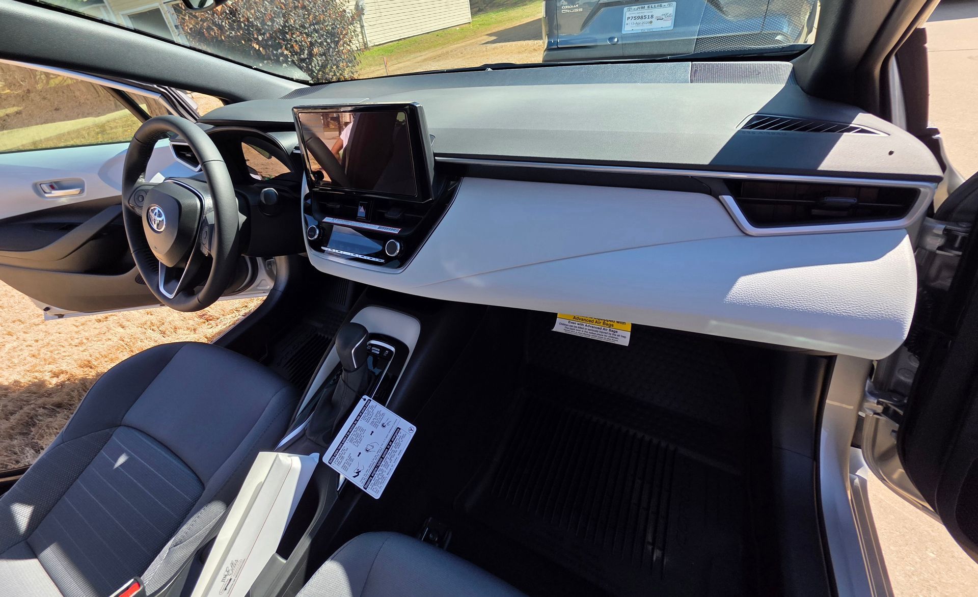 A light gray and black car interior featuring a steering wheel, center touchscreen, and a textured white passenger dash.