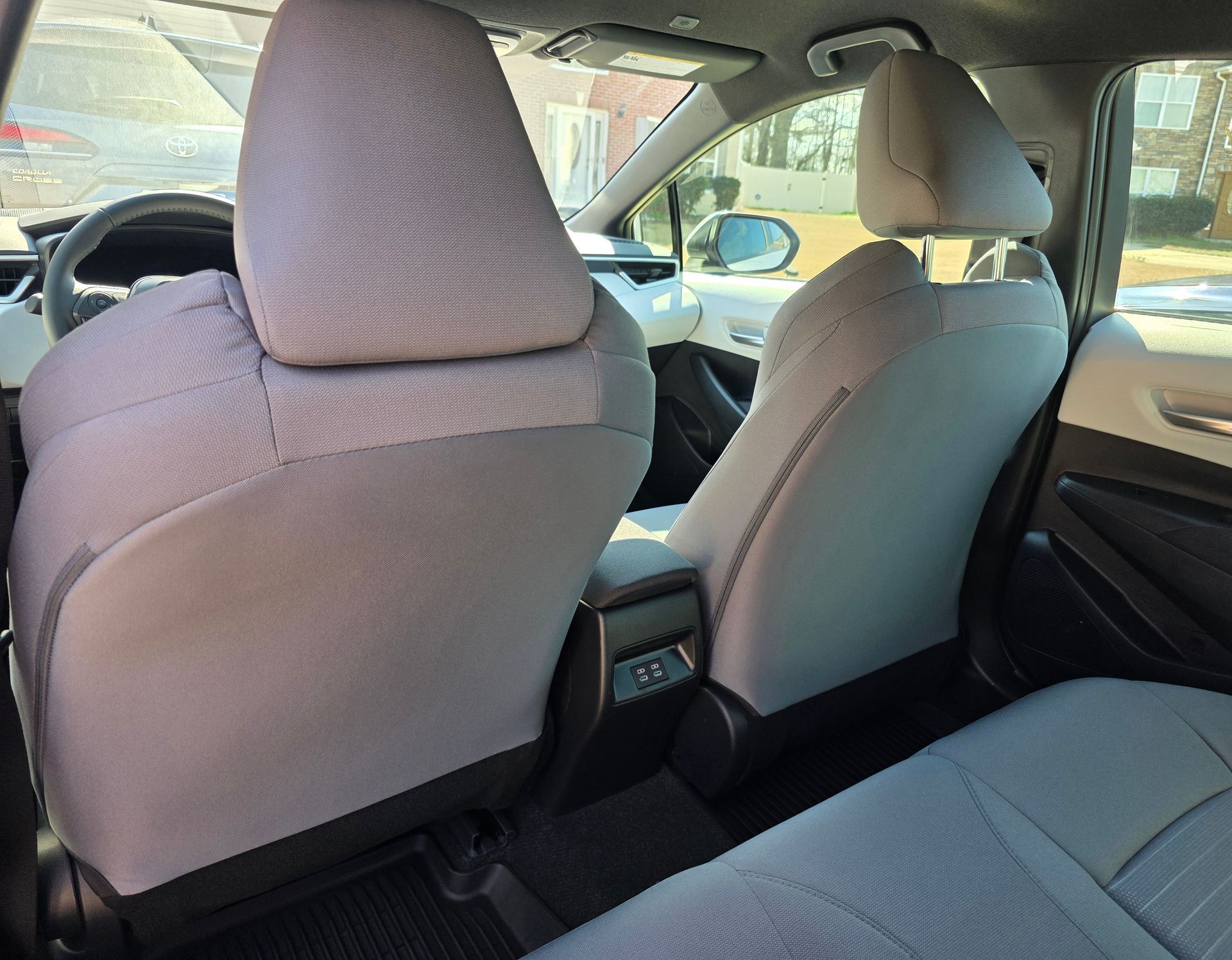The interior of a vehicle seen from the back seat, showing two gray upholstered front seats and a center console.