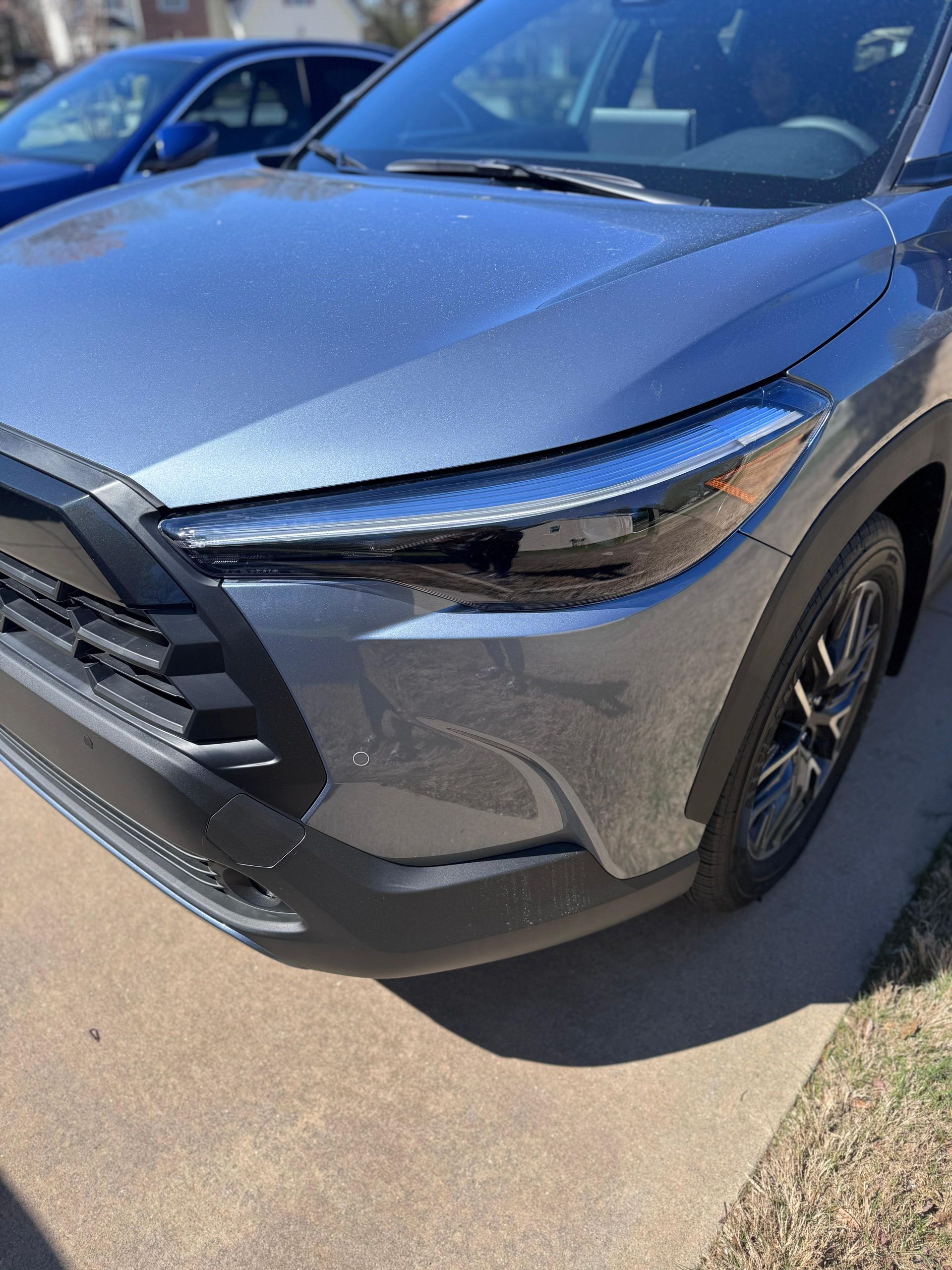 A close-up of the front passenger side of a dark gray SUV parked on a concrete driveway.