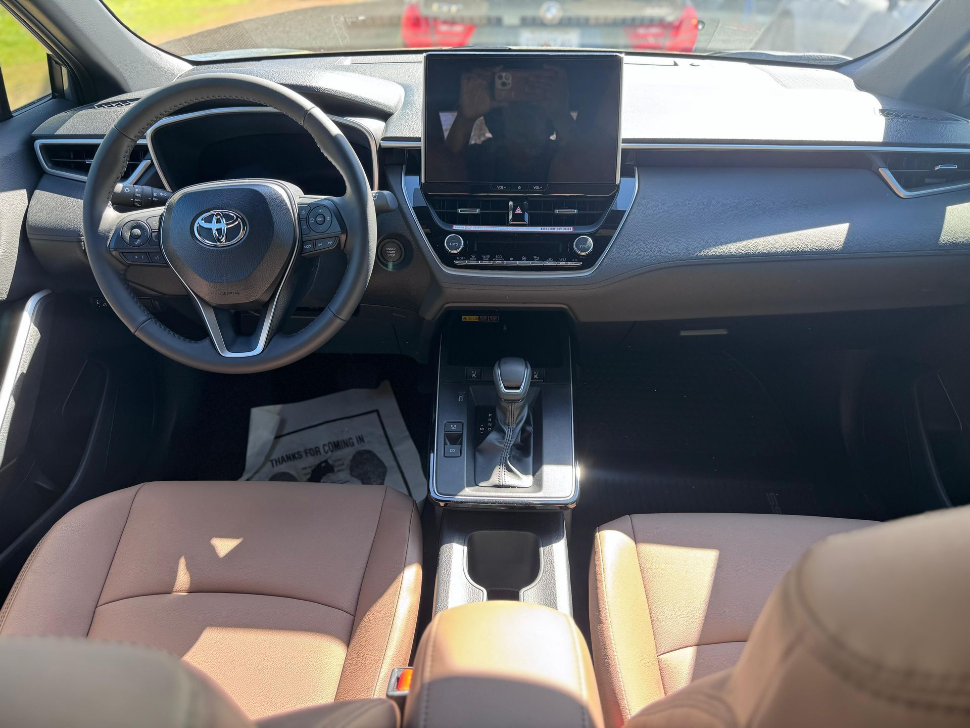 Interior of a vehicle featuring a Toyota steering wheel, touchscreen display, gear shifter, and brown upholstered seats.