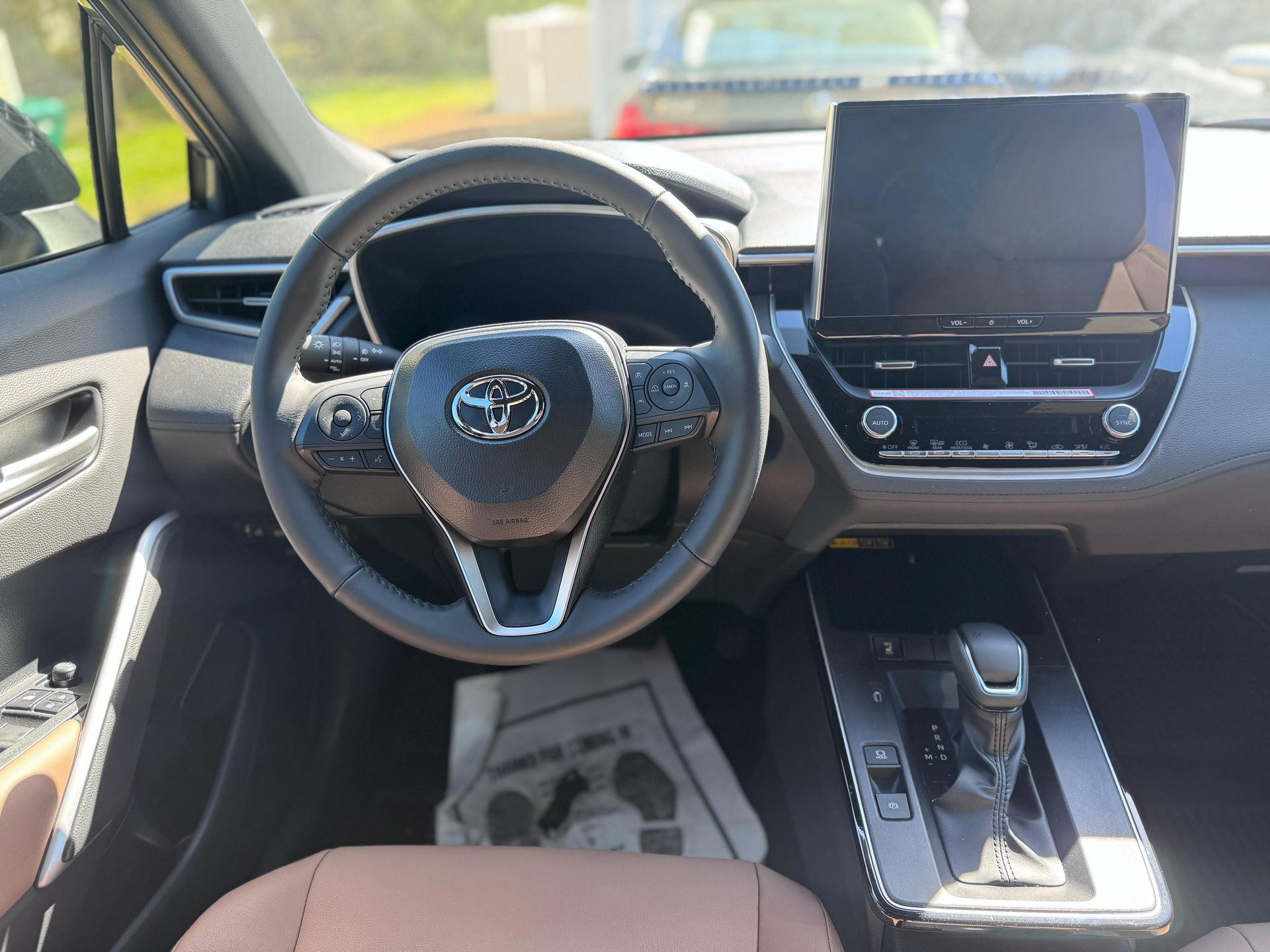 The interior of a Toyota vehicle, featuring a black steering wheel, center console display, and brown seats.
