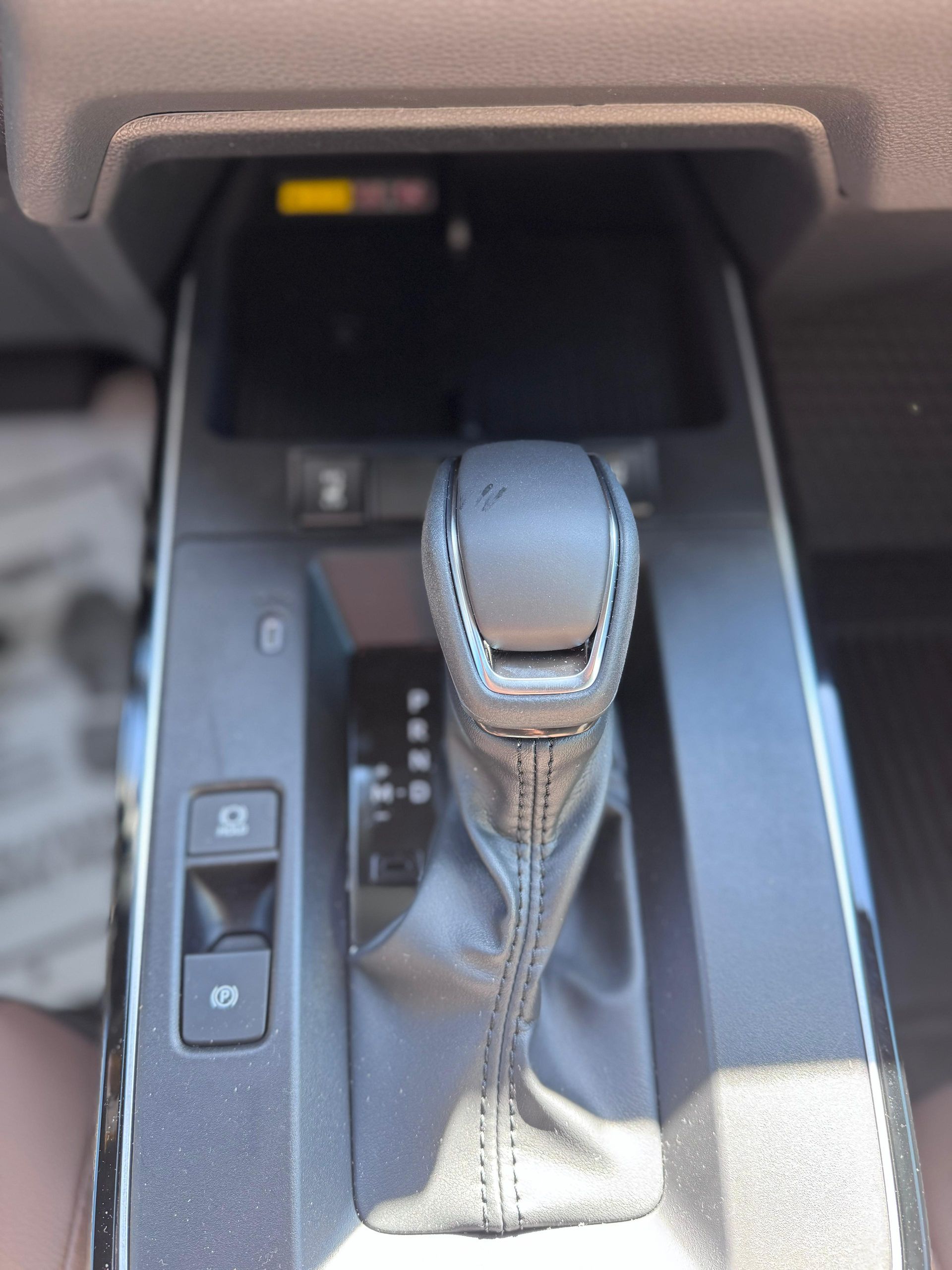 A close-up view of an automatic car gear shifter, along with parking brake and auto-hold buttons on a black console.
