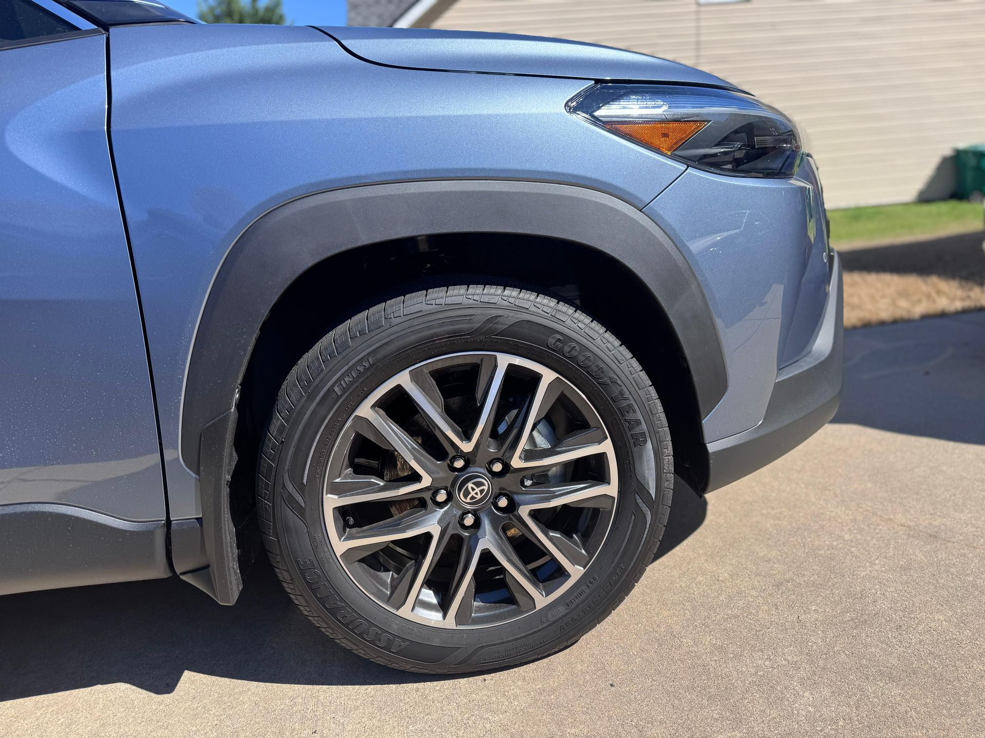 Front side view of a blue SUV with black fender trim and multi-spoke alloy wheels parked on pavement.
